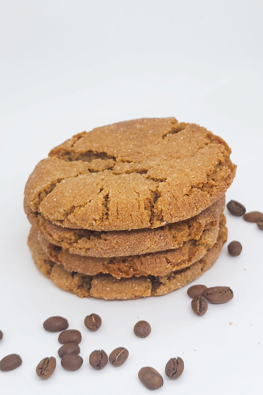 Coffee beans surrounding a stack of three espresso cookies on a white background.