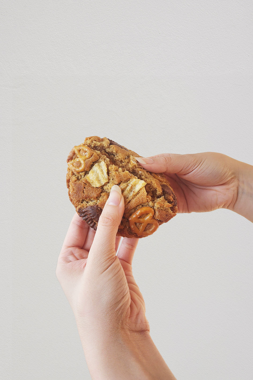 Hand breaking peanut butter cookie with pretzels and potato chips.