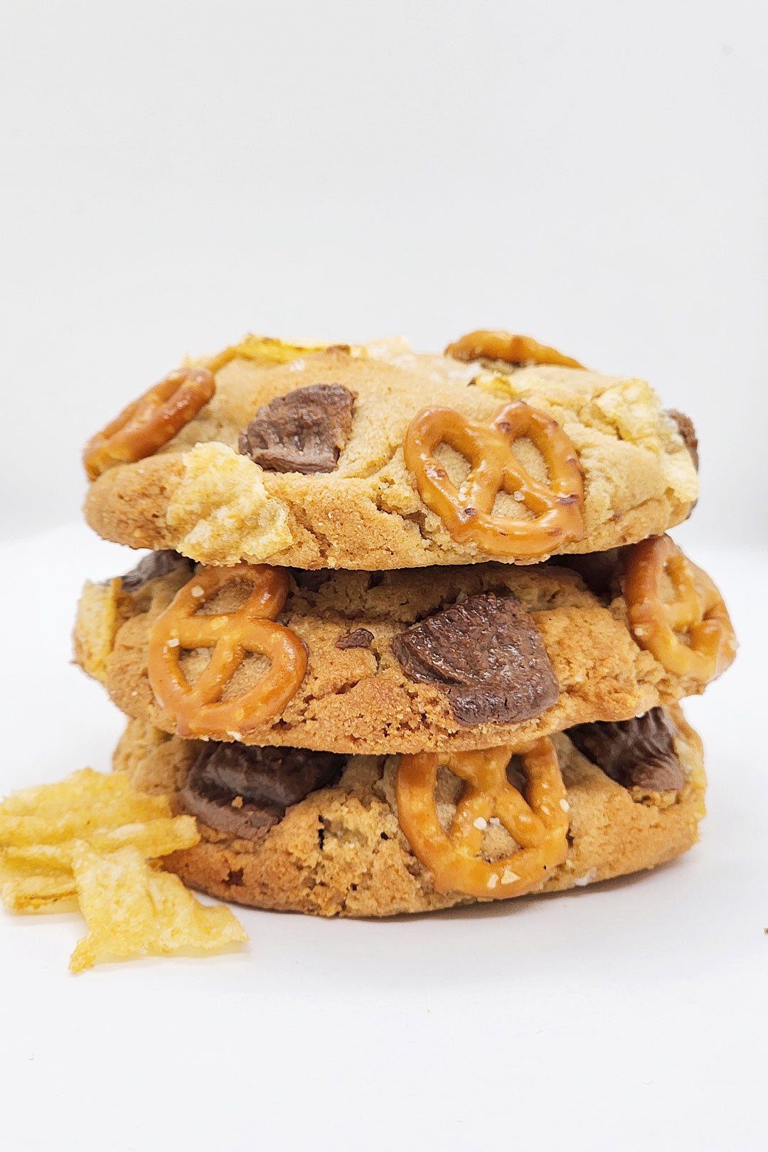 Stack of three peanut butter cookies with peanut butter cups, pretzels and potato chips.