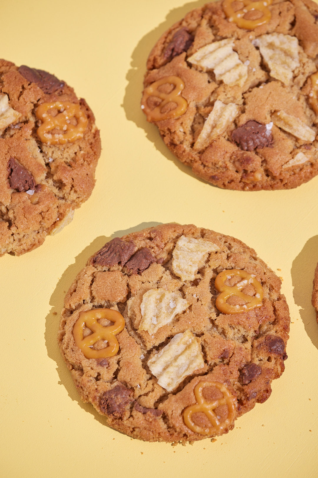 Peanut butter cookie with peanut butter cups, pretzels and potato chips flat lay on a yellow background.